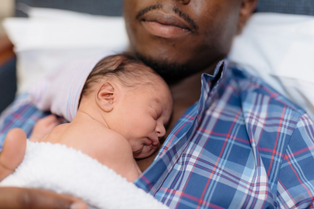 African American father holding newborn baby of chest, skin to skin contact