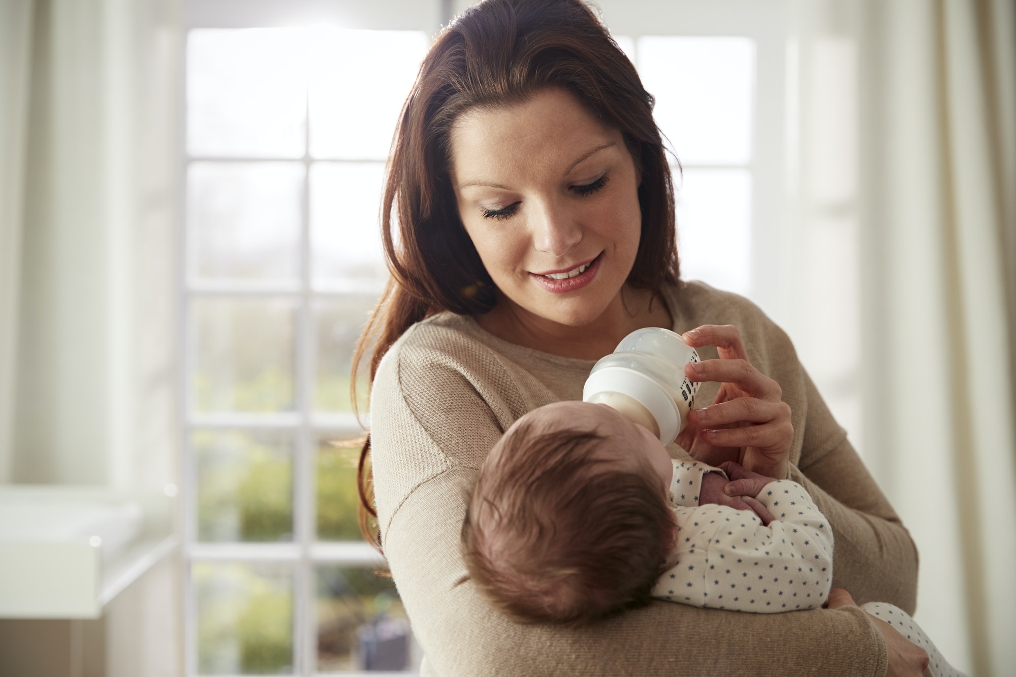 Mother Feeding Newborn Baby From Bottle At Home