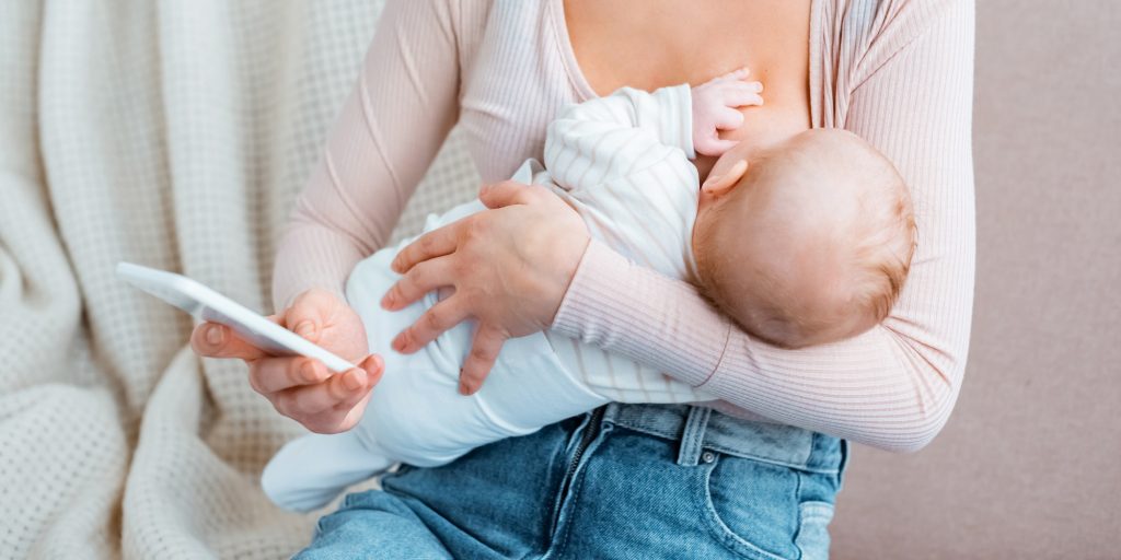 cropped shot of young mother breastfeeding baby and using smartphone