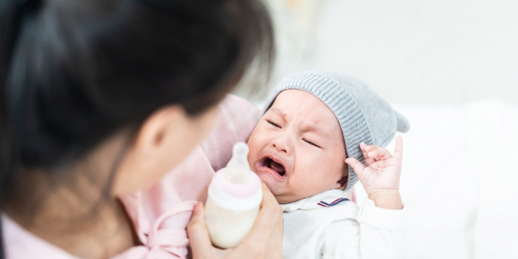 Beautiful Asian mother giving bottle feeding of her breast milk to her crying baby at home.
