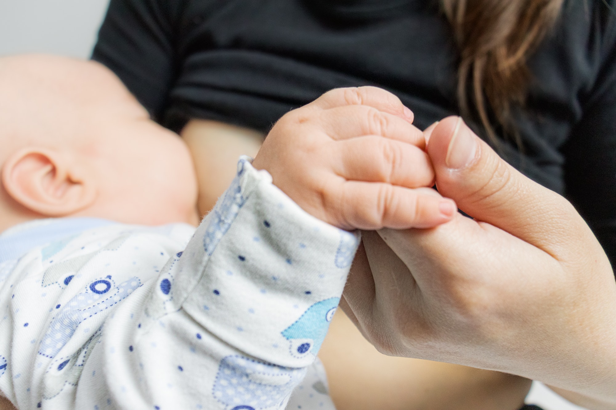 mother holds the baby by the hand while breastfeeding. breastfeeding, mother and baby at home.