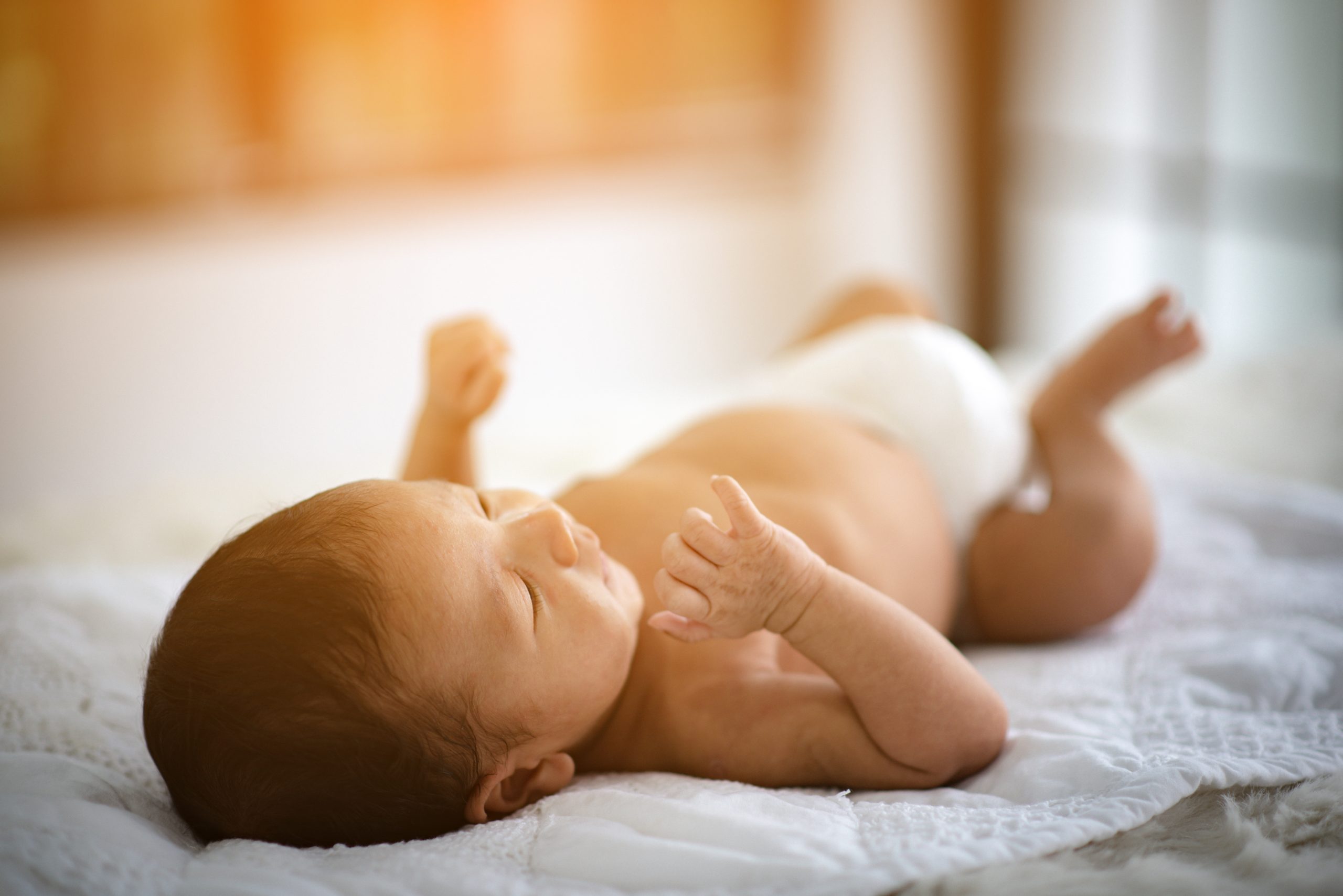 newborn baby lying on bed with light shining through window