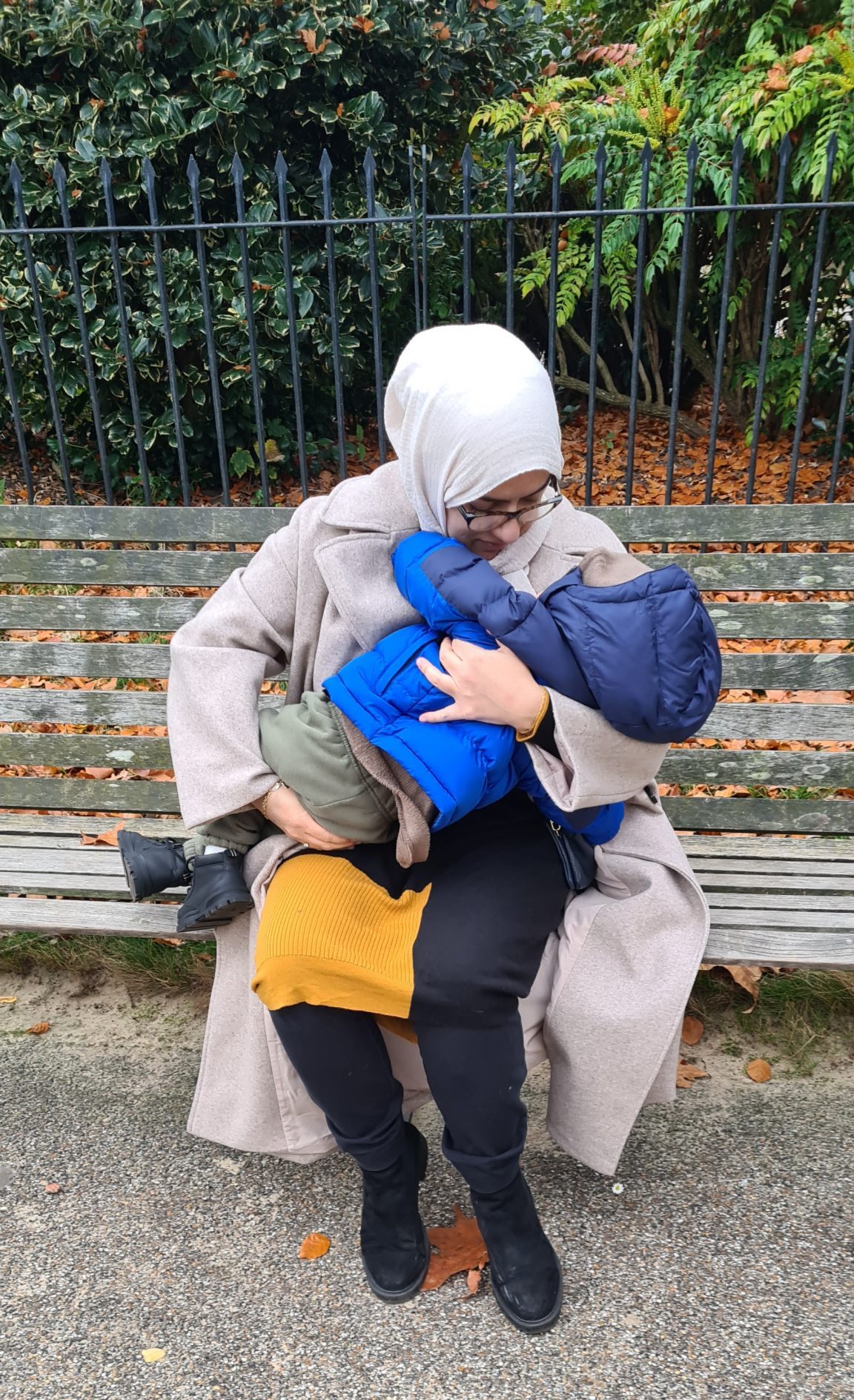 Houda breastfeeding her toddler son outside on a bench