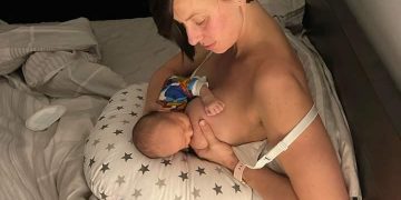 Breastfeeding mother using feeding pillow to breastfed newborn baby in bed