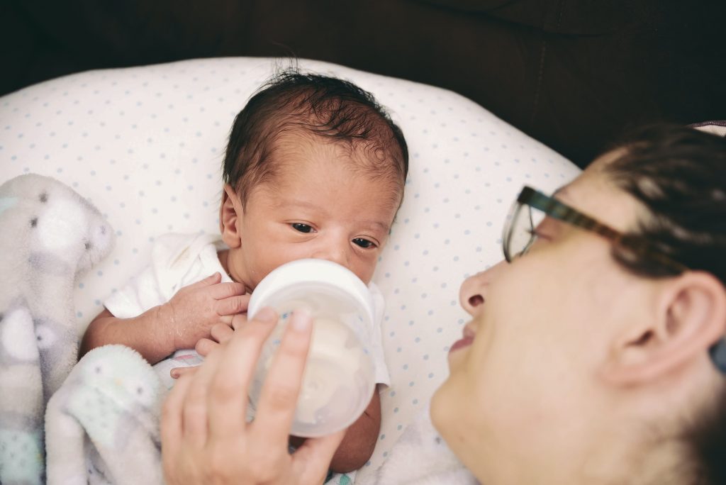 Young millennial mother feeding diverse mixed race newborn baby boy formula from bottle