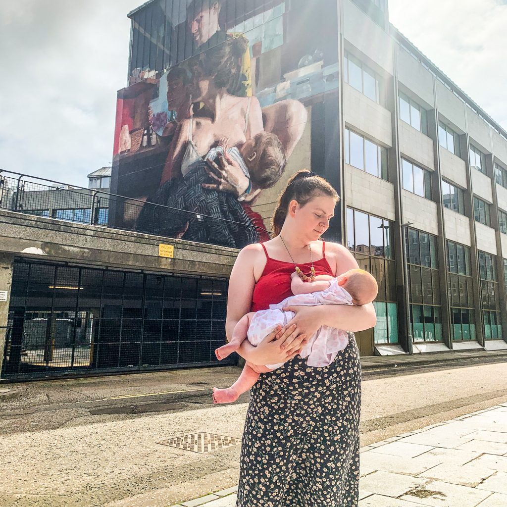 Elle Phelan breastfeeding in public in-front of a breastfeeding mural