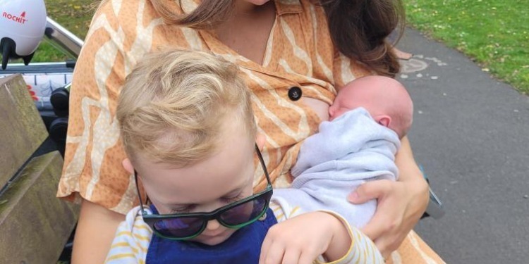 Grace breastfeeds her son whilst holding her toddler son