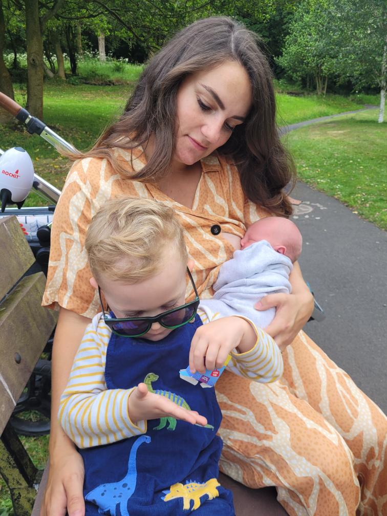 Grace breastfeeds her son whilst holding her toddler son