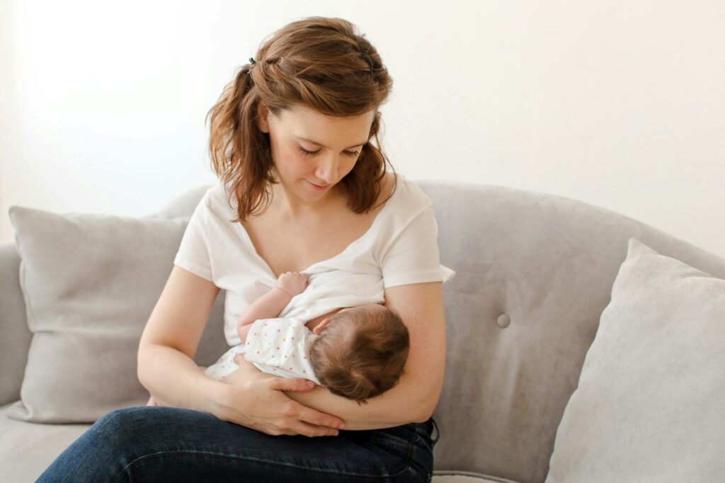 Happy mother breastfeeding baby sitting on sofa