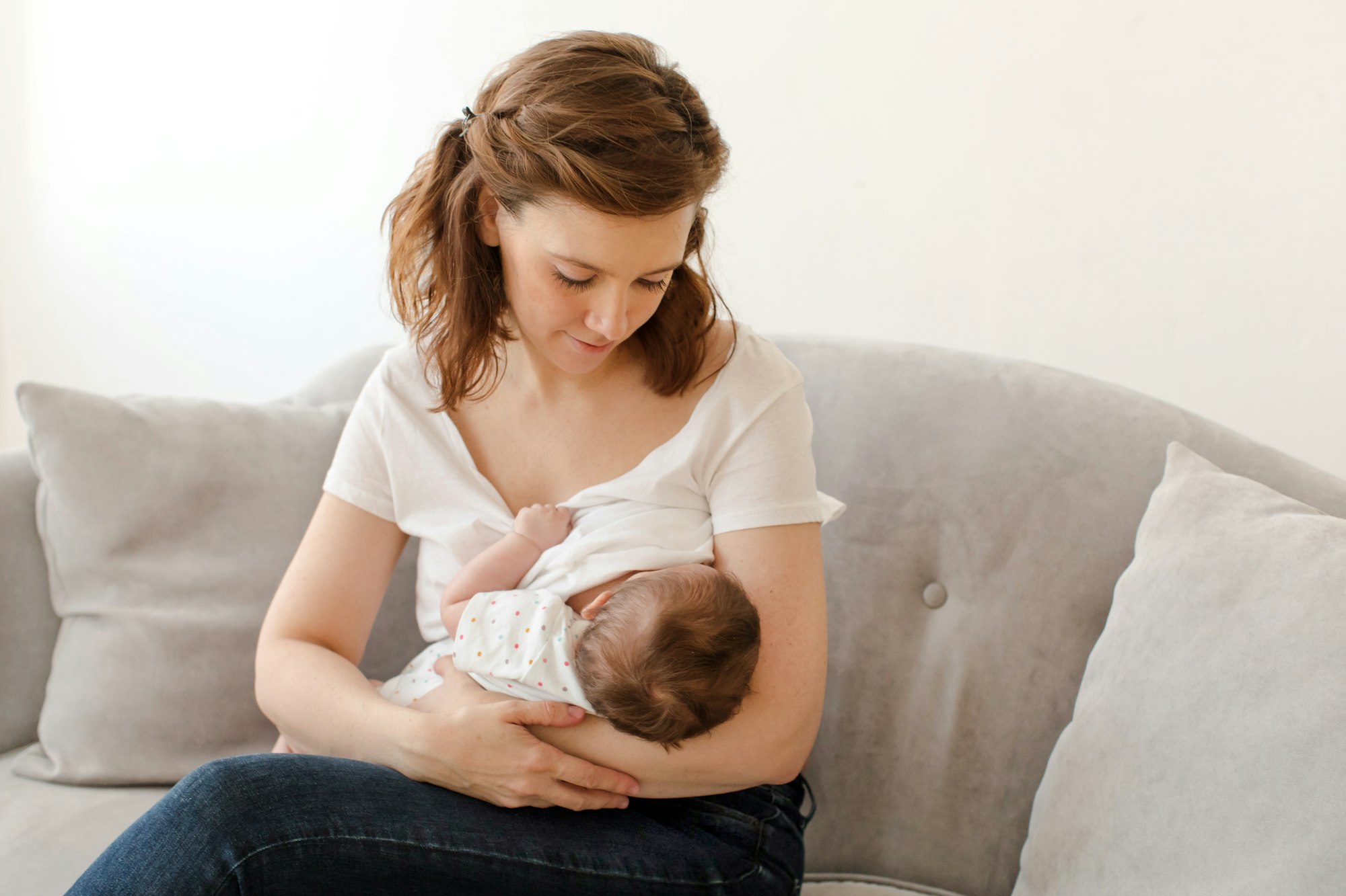 Happy mother breastfeeding baby sitting on sofa