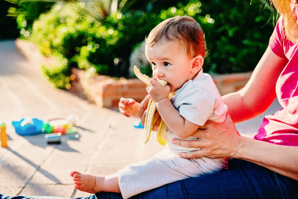 Baby in her mother's arms learning to eat solid foods like raw fruit, blw.