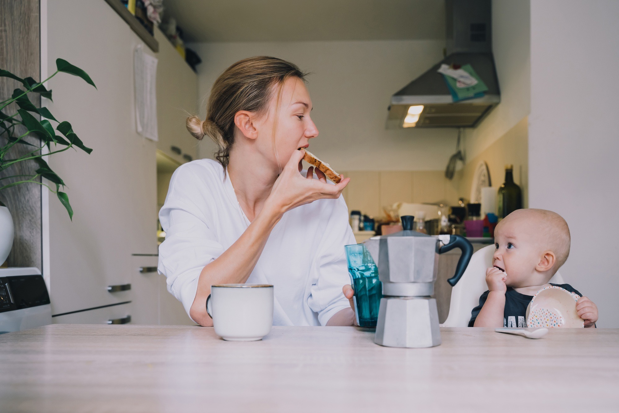 Loving smiling mother and baby eating breakfast and have fun in kitchen at home.