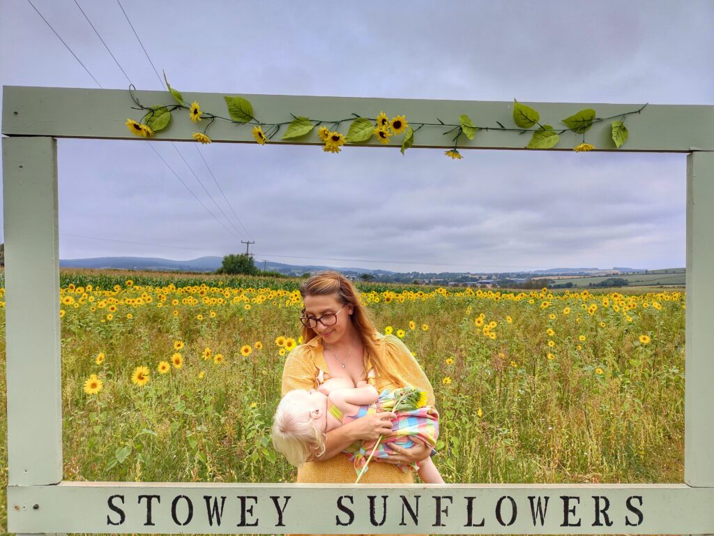 Kiana Van Kempen breastfeeding amongst the sunflowers