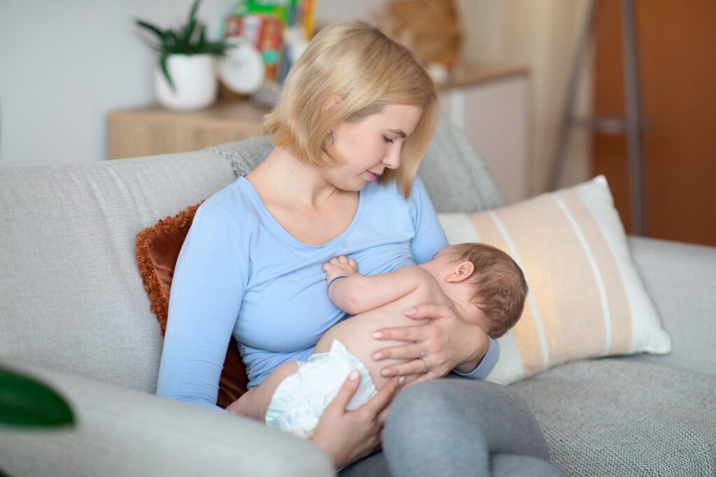 Beautiful blonde woman holding her little kid, breastfeeding