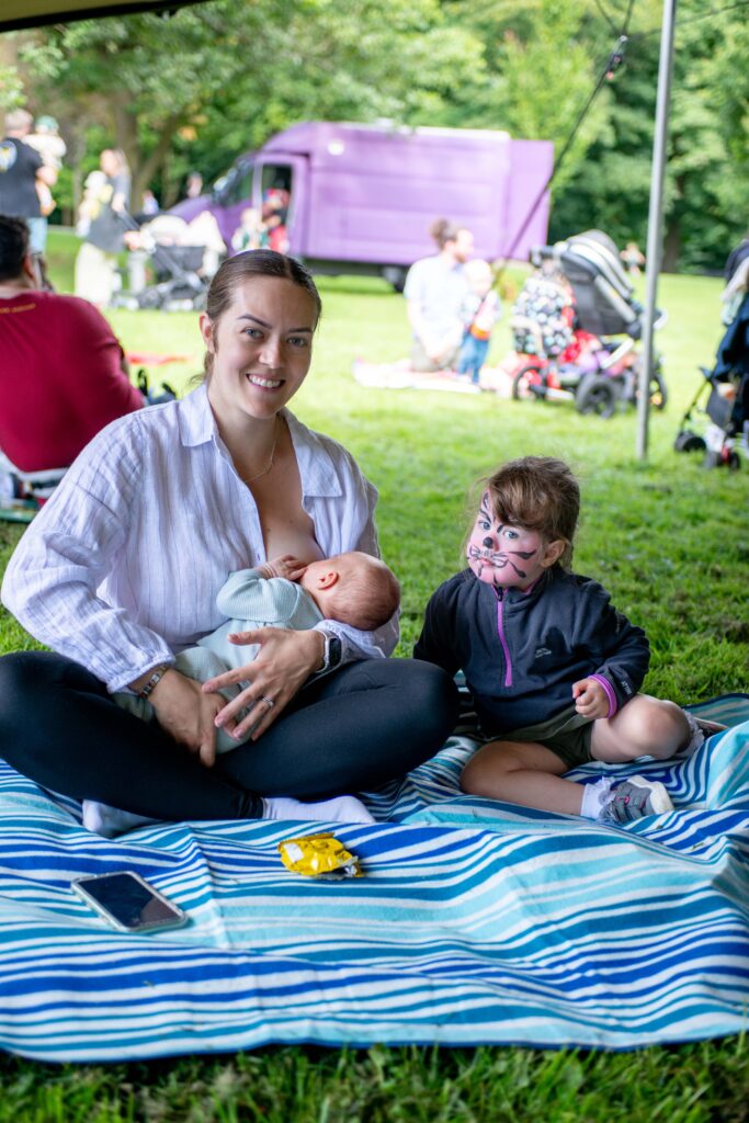 Mother breastfeeding baby at Breastival with toddler beside her